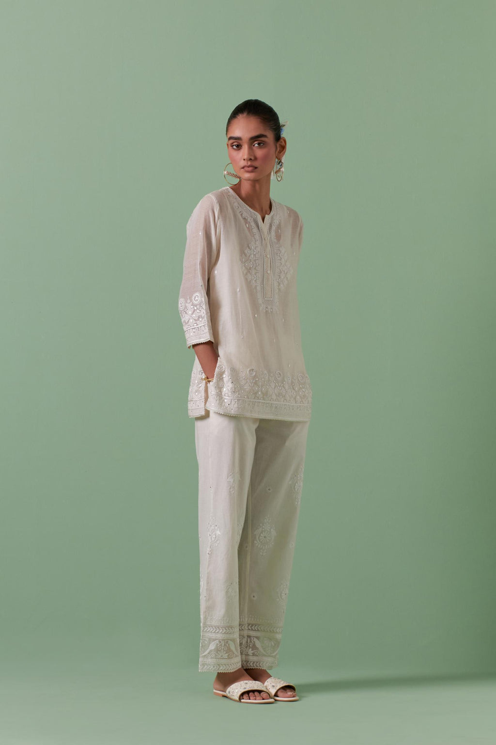 Off-white cotton chanderi embroidered short top with 3/4th sleeves, paired with off white cotton straight pants with all over off white color embroidery detailed with sequins.