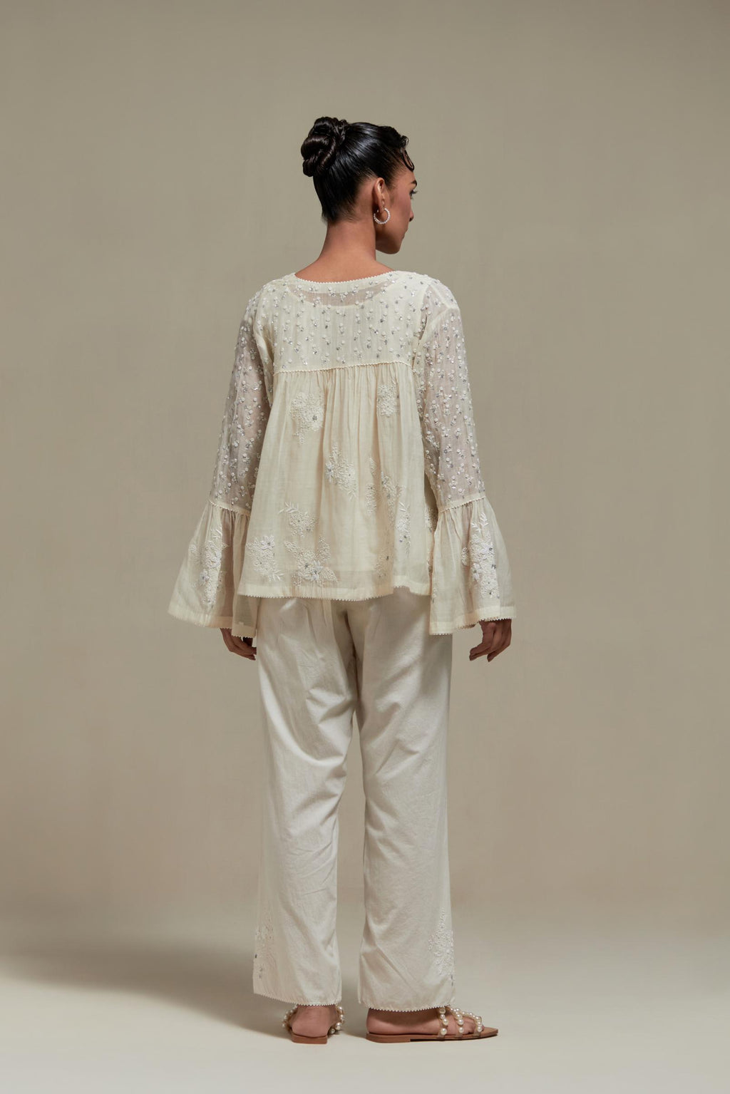 Off white cotton Chanderi short top with appliqué motifs and delicate embroidered flowers, highlighted with sequins and beads, paired with Off white straight pants with appliqué motifs at the sides, highlighted with sequins and beads.