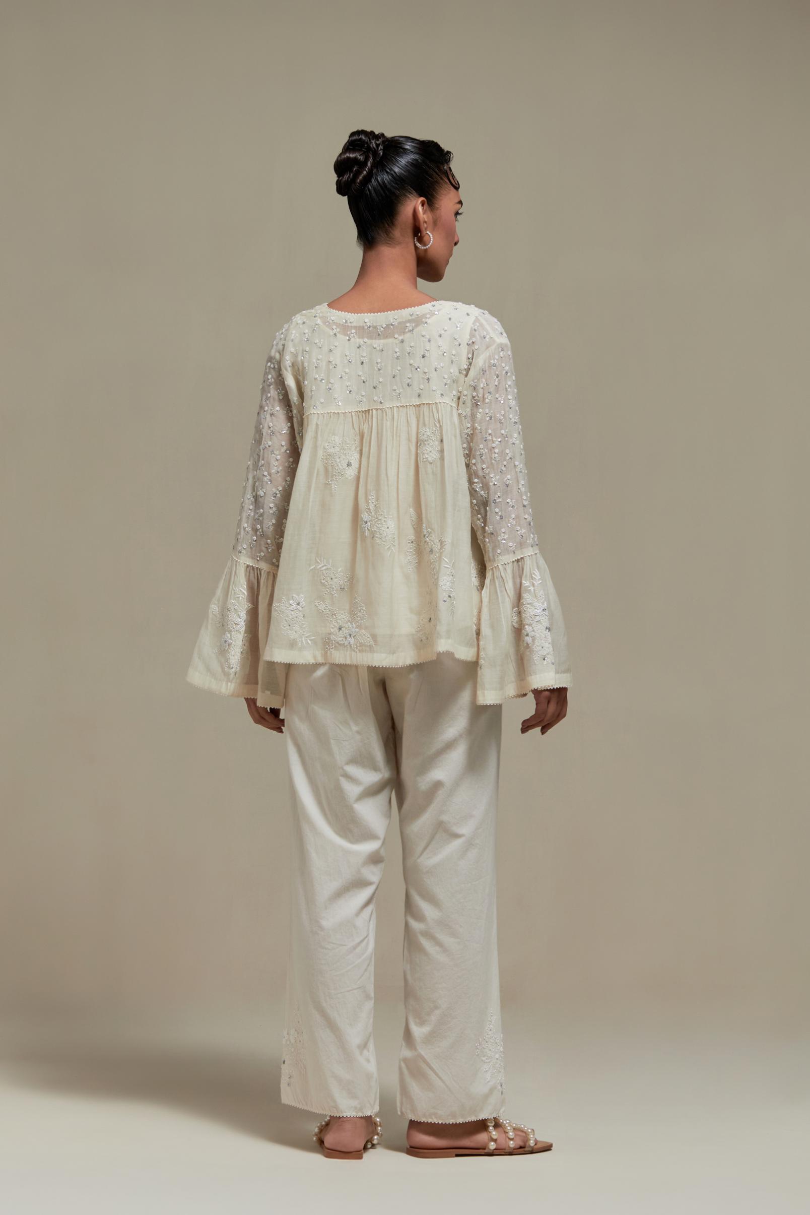 Off white cotton Chanderi short top with appliqué motifs and delicate embroidered flowers, highlighted with sequins and beads, paired with Off white straight pants with appliqué motifs at the sides, highlighted with sequins and beads.