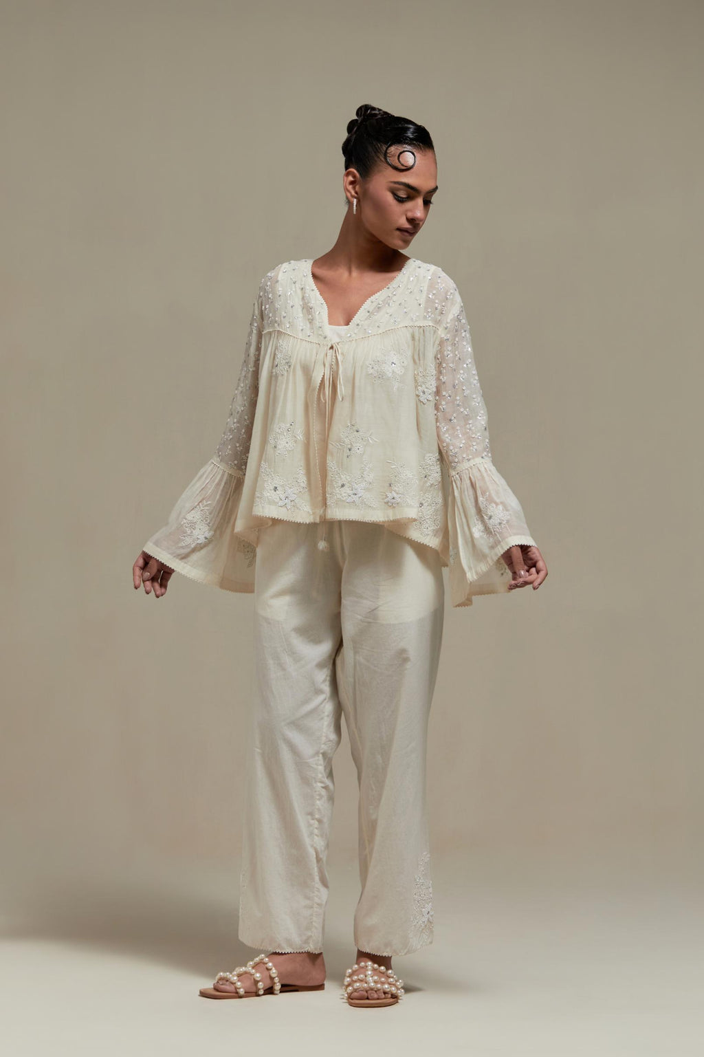 Off white cotton Chanderi short top with appliqué motifs and delicate embroidered flowers, highlighted with sequins and beads, paired with Off white straight pants with appliqué motifs at the sides, highlighted with sequins and beads.