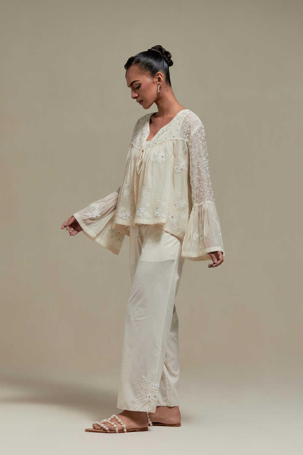 Off white cotton Chanderi short top with appliqué motifs and delicate embroidered flowers, highlighted with sequins and beads, paired with Off white straight pants with appliqué motifs at the sides, highlighted with sequins and beads.