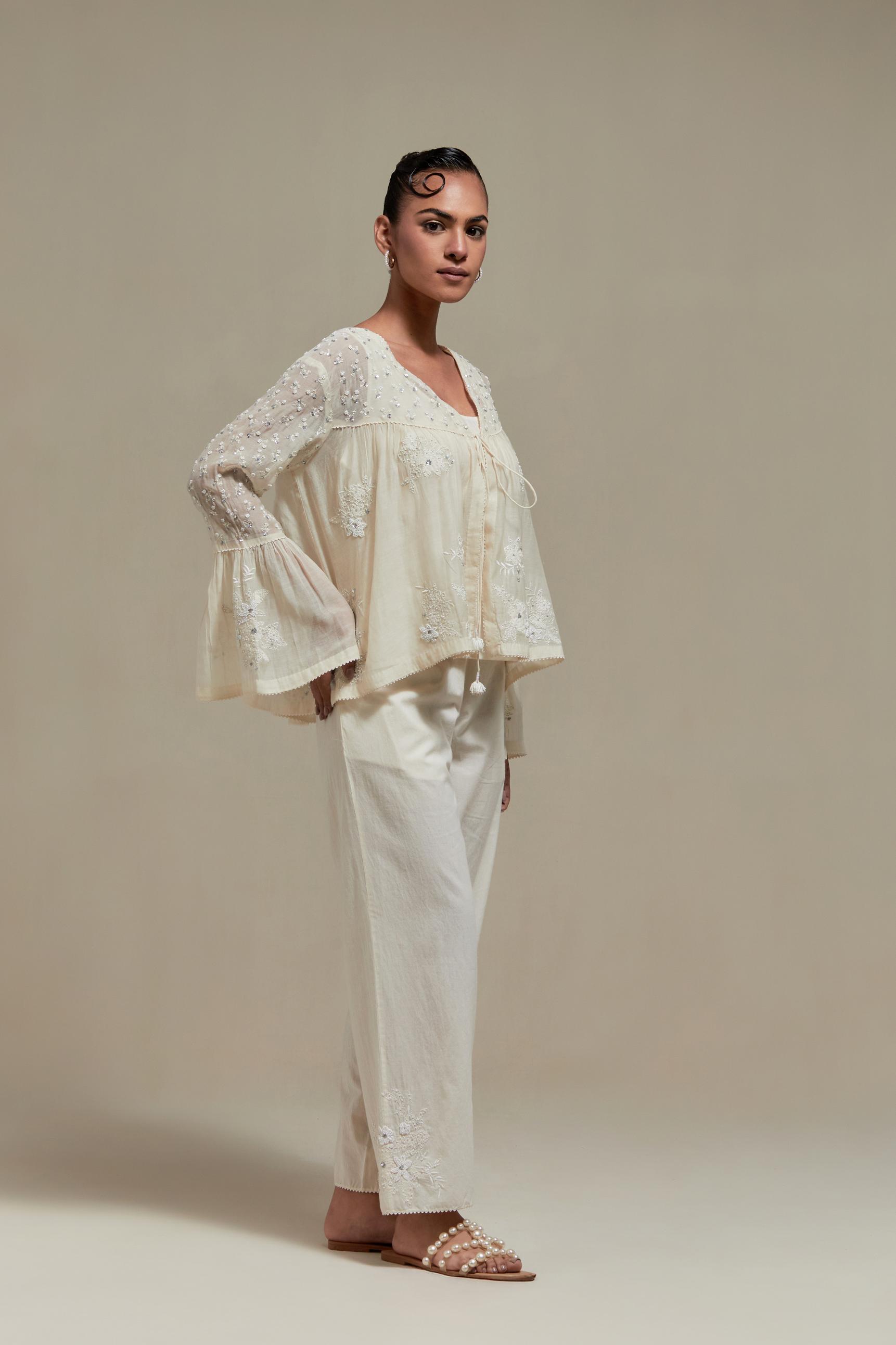 Off white cotton Chanderi short top with appliqué motifs and delicate embroidered flowers, highlighted with sequins and beads, paired with Off white straight pants with appliqué motifs at the sides, highlighted with sequins and beads.