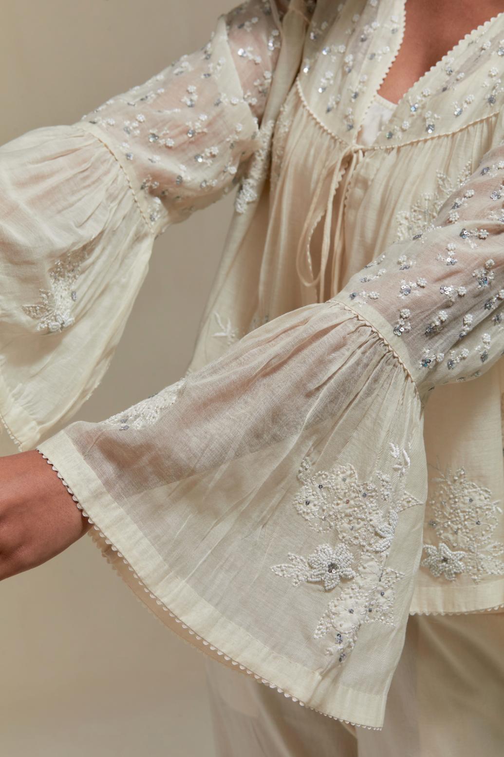 Off white cotton Chanderi short top with appliqué motifs and delicate embroidered flowers, highlighted with sequins and beads, paired with Off white straight pants with appliqué motifs at the sides, highlighted with sequins and beads.