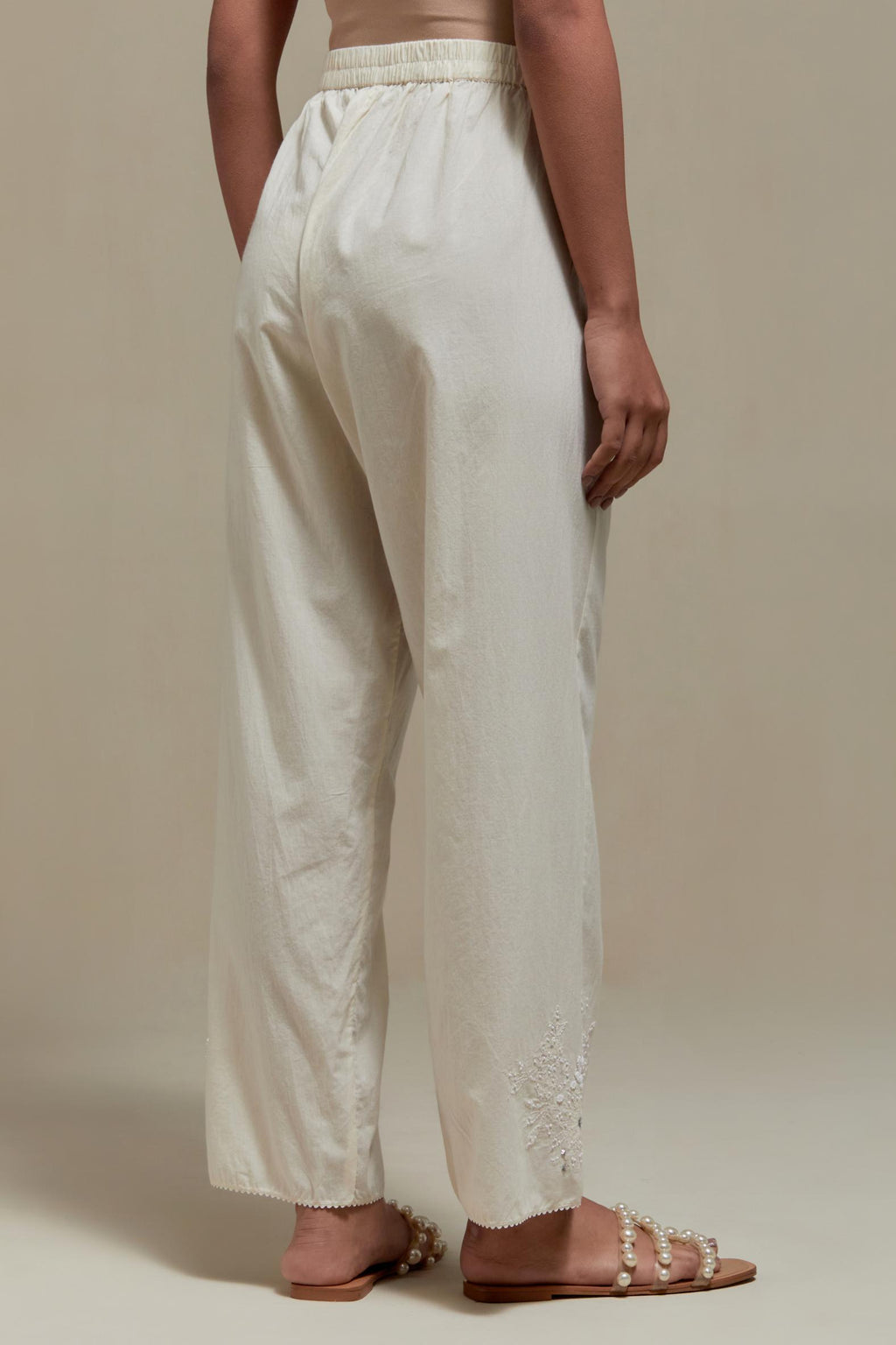 Off white straight pants with appliqué motifs at the sides, highlighted with sequins and beads.