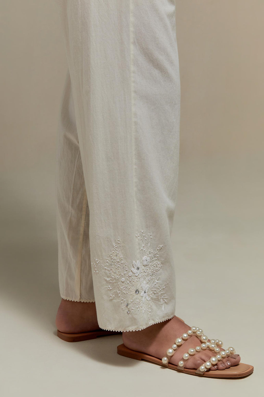 Off white straight pants with appliqué motifs at the sides, highlighted with sequins and beads.