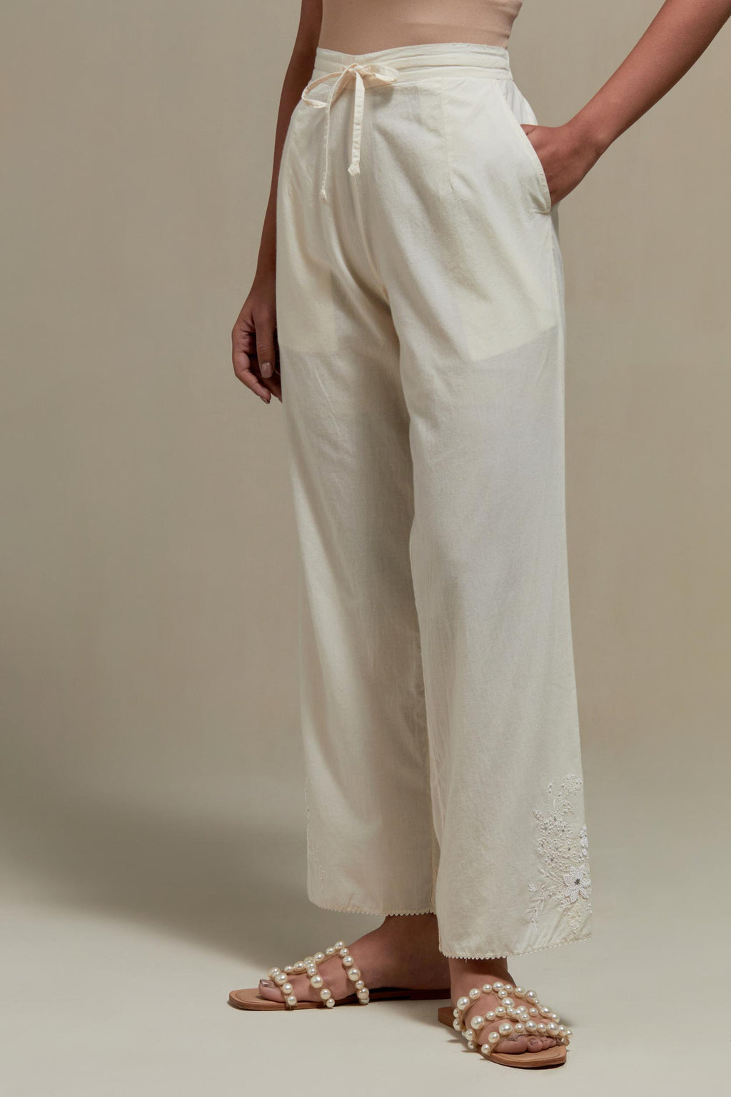 Off white straight pants with appliqué motifs at the sides, highlighted with sequins and beads.