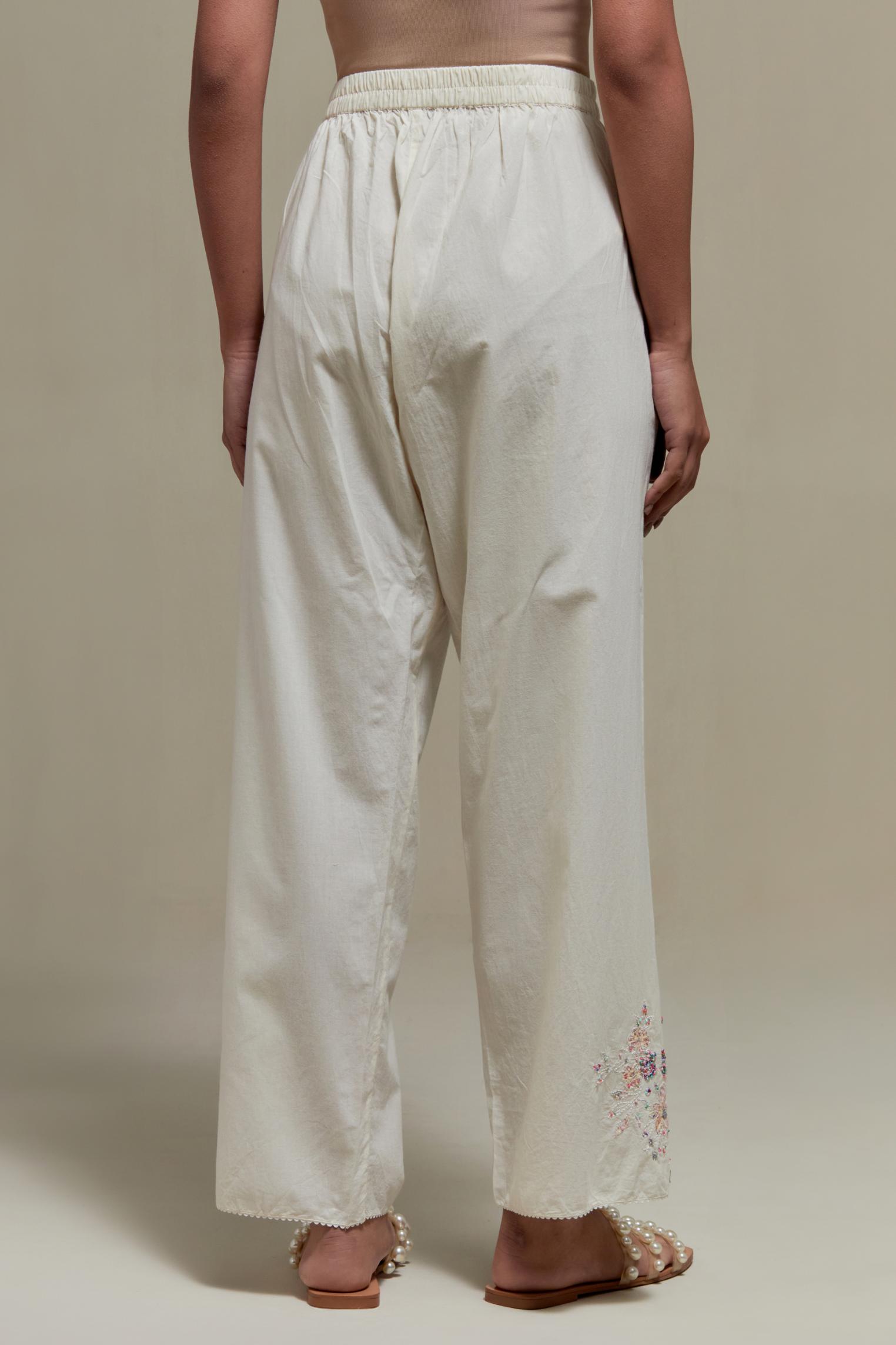 Off white straight pants with pink & beige hand block printed appliqué motifs at the sides, highlighted with sequins and multi coloured beads.
