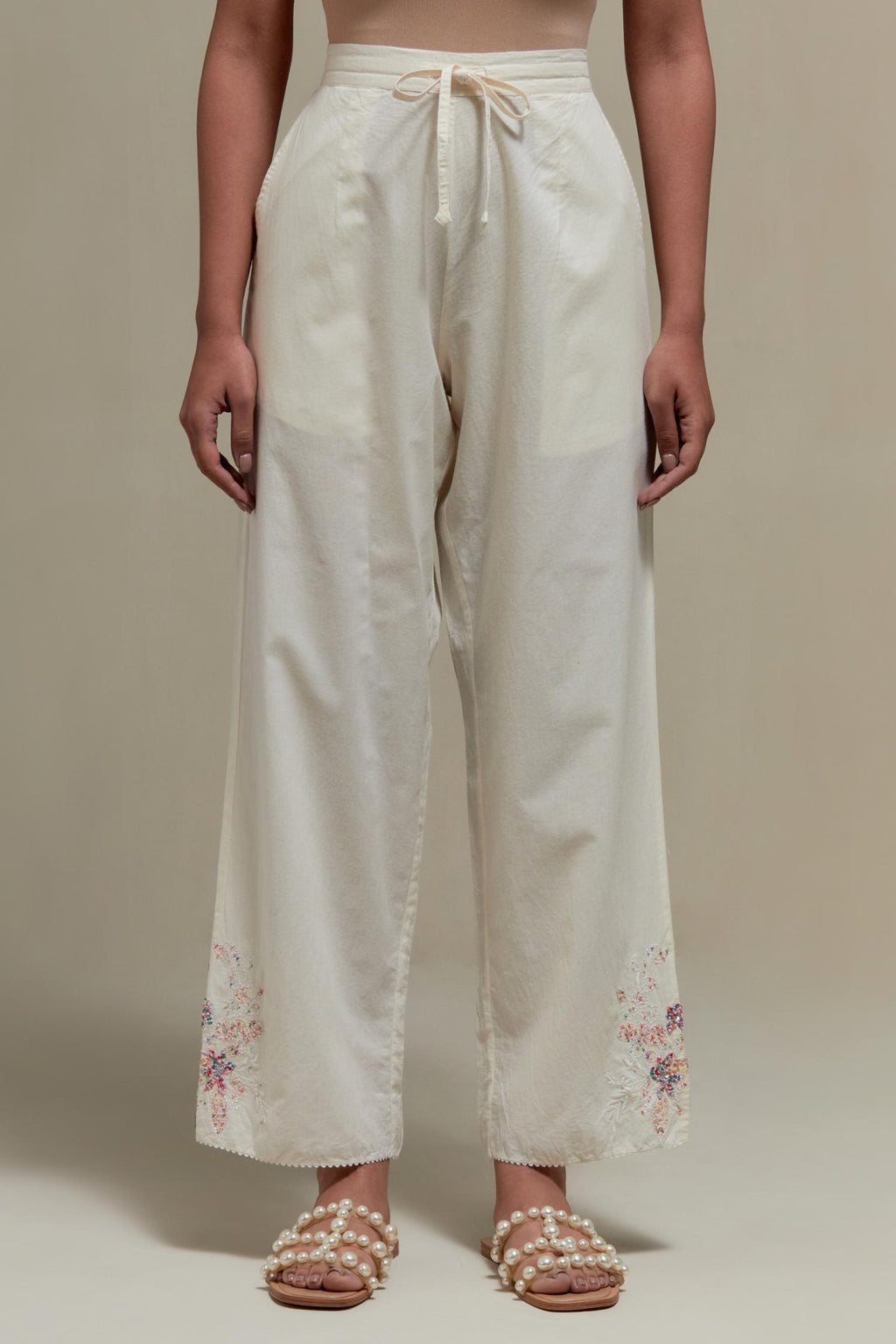 Off white straight pants with pink & beige hand block printed appliqué motifs at the sides, highlighted with sequins and multi coloured beads.