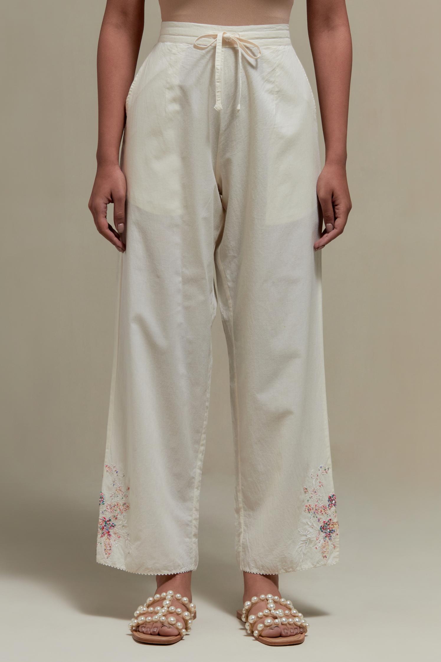 Off white straight pants with pink & beige hand block printed appliqué motifs at the sides, highlighted with sequins and multi coloured beads.