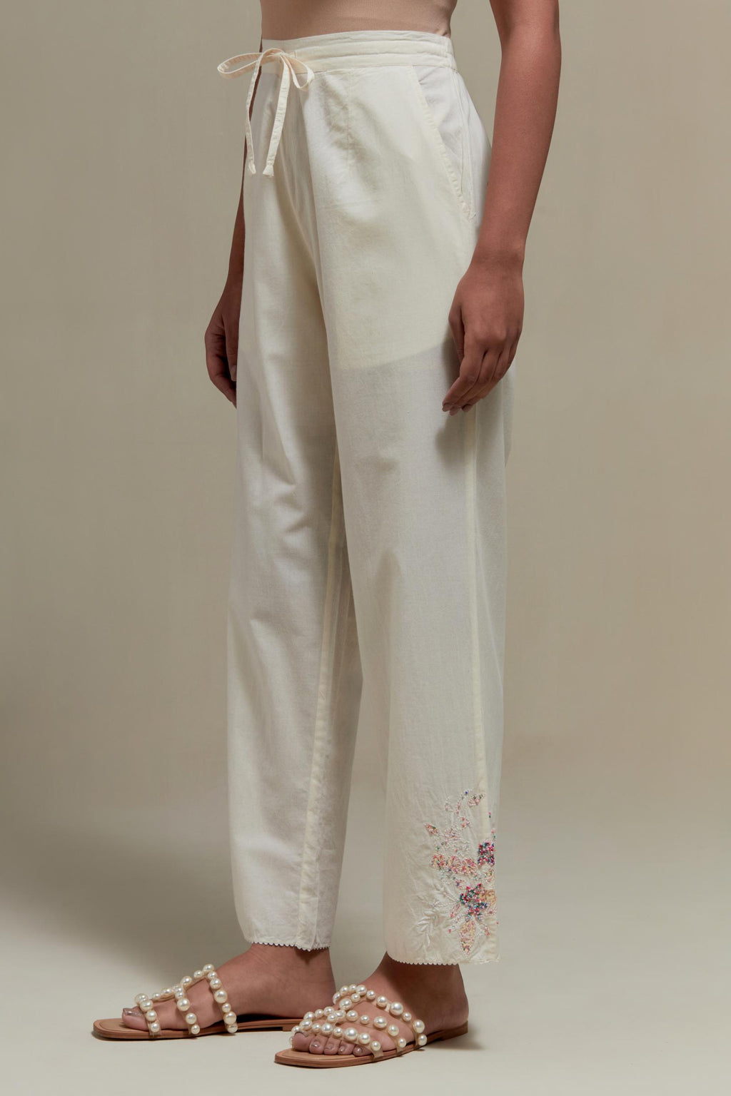 Off white straight pants with pink & beige hand block printed appliqué motifs at the sides, highlighted with sequins and multi coloured beads.