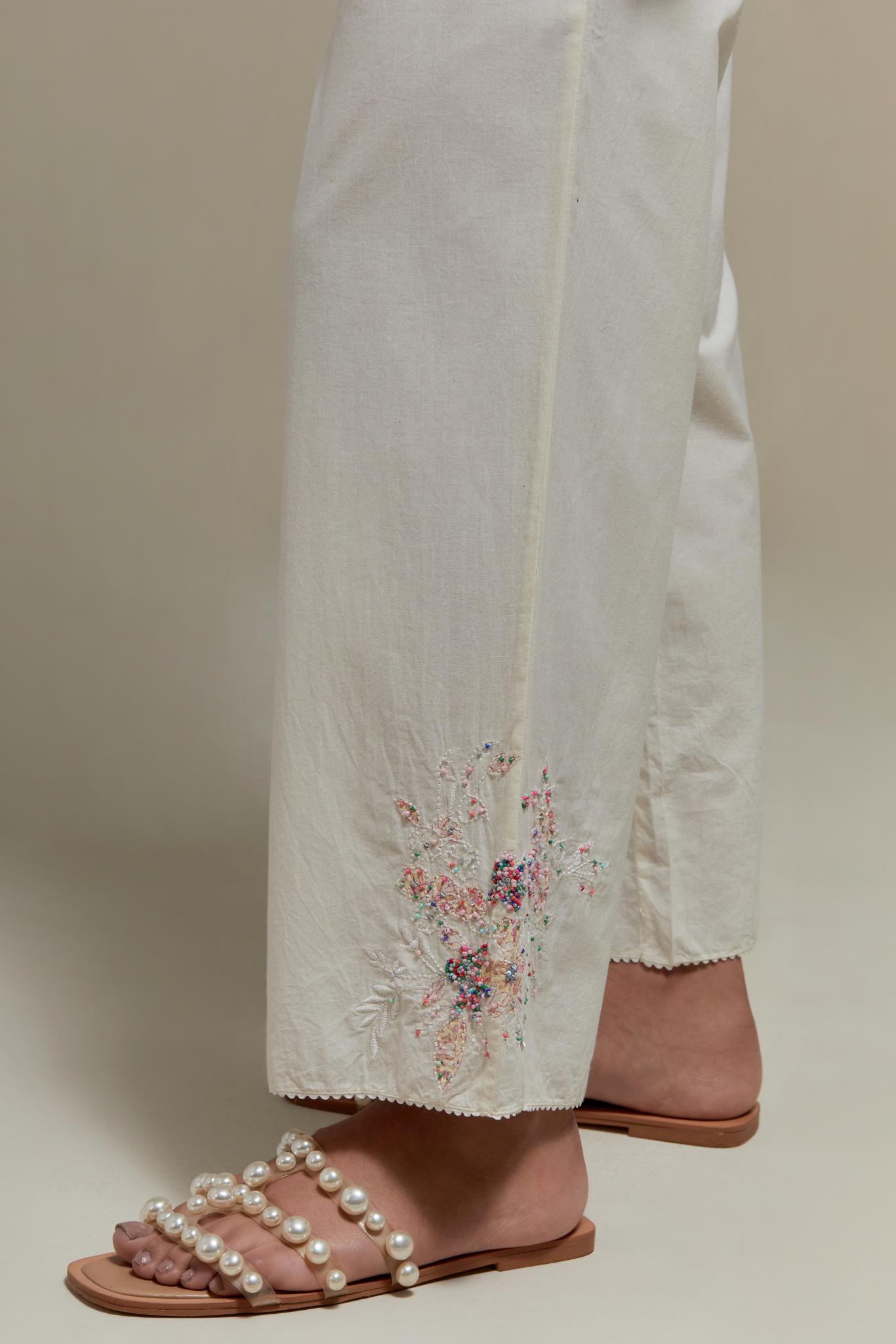 Off white straight pants with pink & beige hand block printed appliqué motifs at the sides, highlighted with sequins and multi coloured beads.