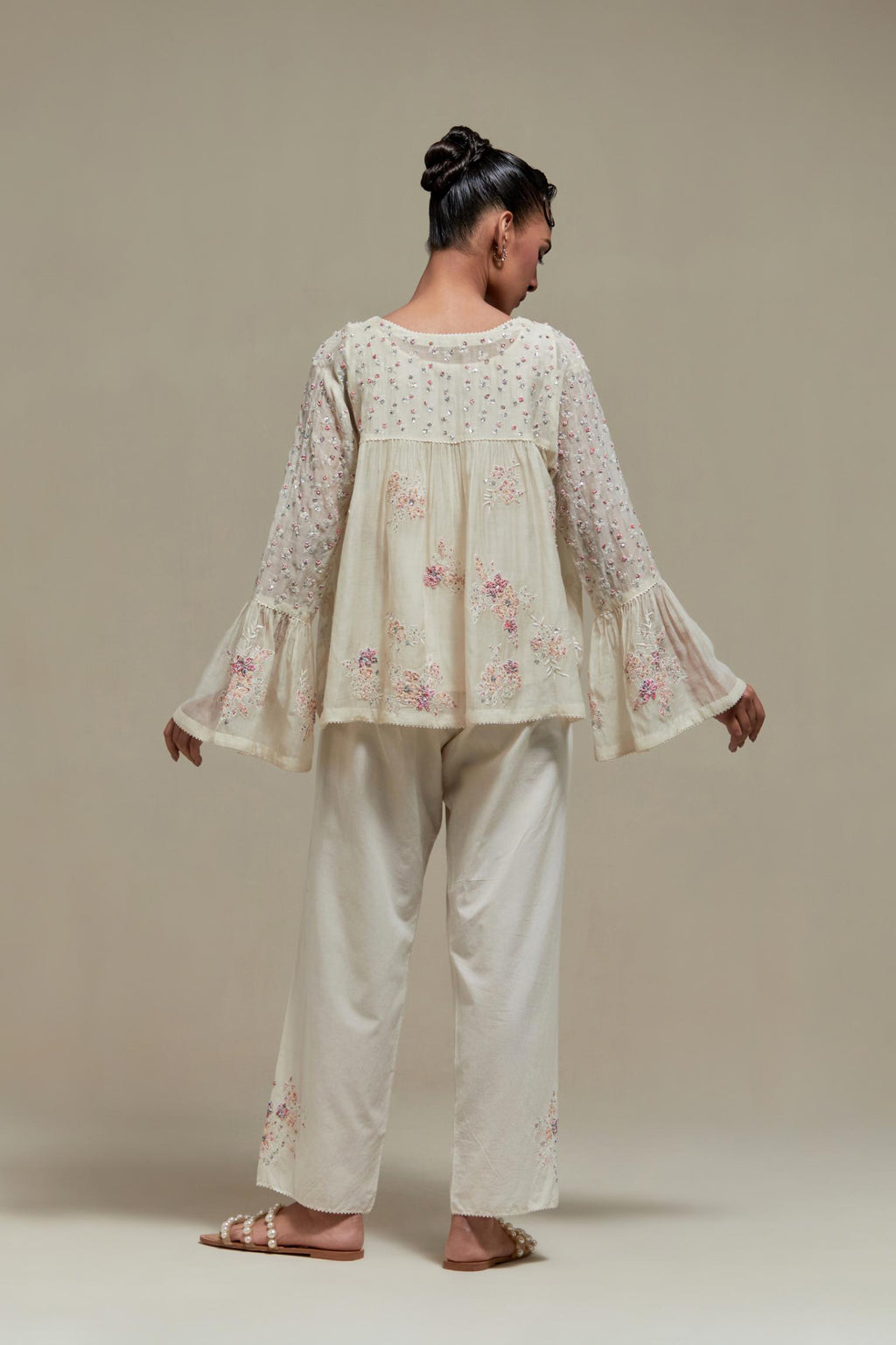 Off-white cotton Chanderi short top featuring pink & beige block print appliqué, floral embroidery, and beadwork. Paired with matching straight pants with side appliqué and sequin highlights. Ideal for elegant, light wear.