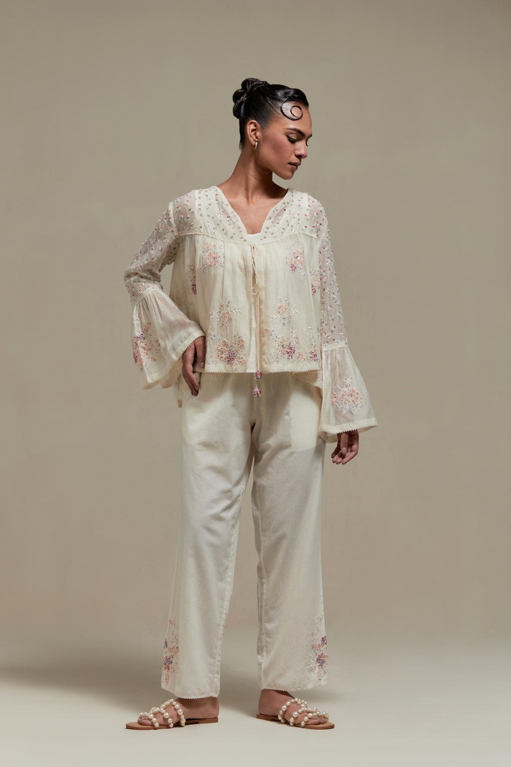 Off-white cotton Chanderi short top featuring pink & beige block print appliqué, floral embroidery, and beadwork. Paired with matching straight pants with side appliqué and sequin highlights. Ideal for elegant, light wear.