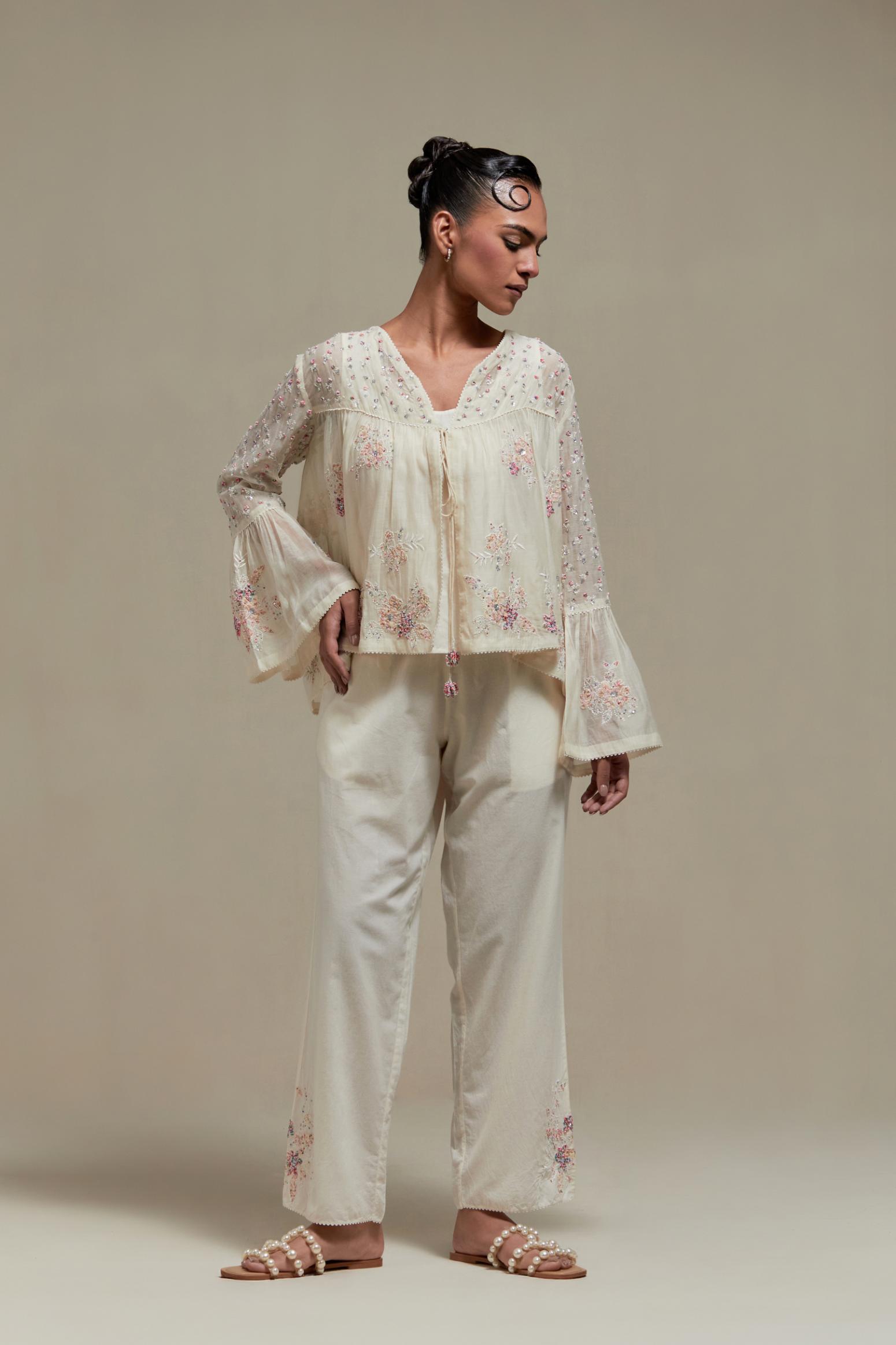 Off-white cotton Chanderi short top featuring pink & beige block print appliqué, floral embroidery, and beadwork. Paired with matching straight pants with side appliqué and sequin highlights. Ideal for elegant, light wear.