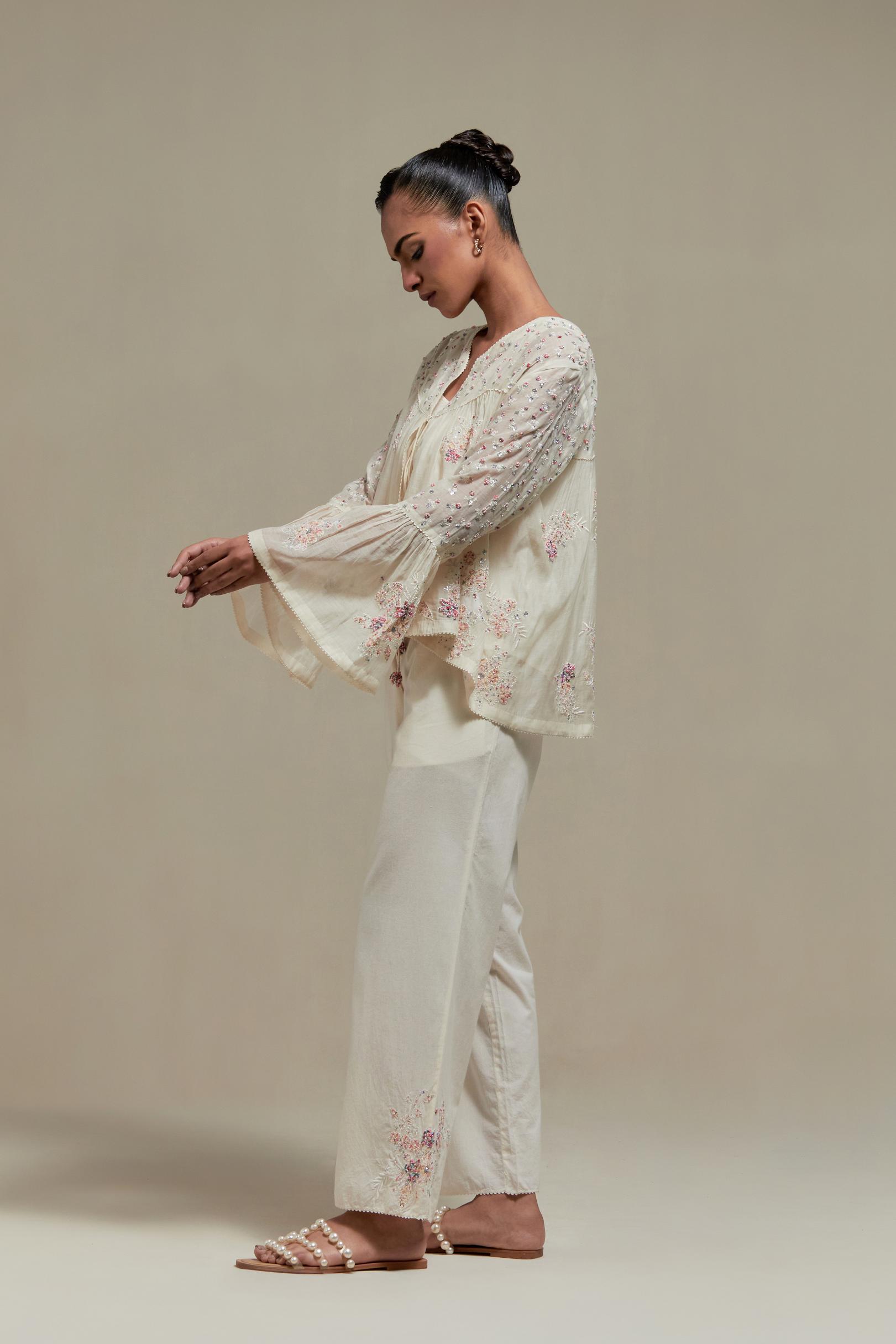 Off-white cotton Chanderi short top featuring pink & beige block print appliqué, floral embroidery, and beadwork. Paired with matching straight pants with side appliqué and sequin highlights. Ideal for elegant, light wear.