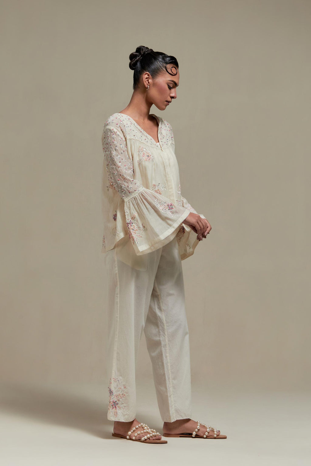 Off-white cotton Chanderi short top featuring pink & beige block print appliqué, floral embroidery, and beadwork. Paired with matching straight pants with side appliqué and sequin highlights. Ideal for elegant, light wear.