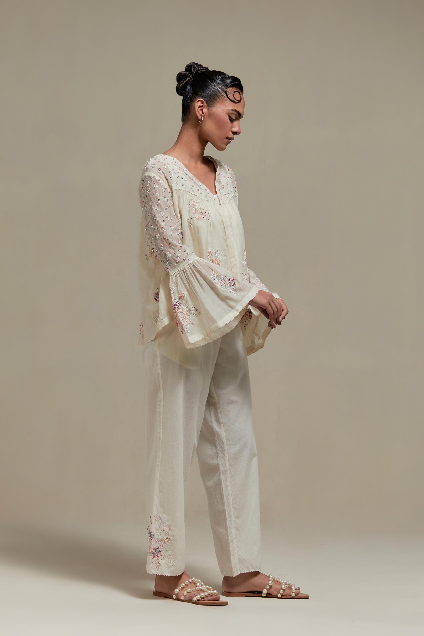 Off-white cotton Chanderi short top featuring pink & beige block print appliqué, floral embroidery, and beadwork. Paired with matching straight pants with side appliqué and sequin highlights. Ideal for elegant, light wear.