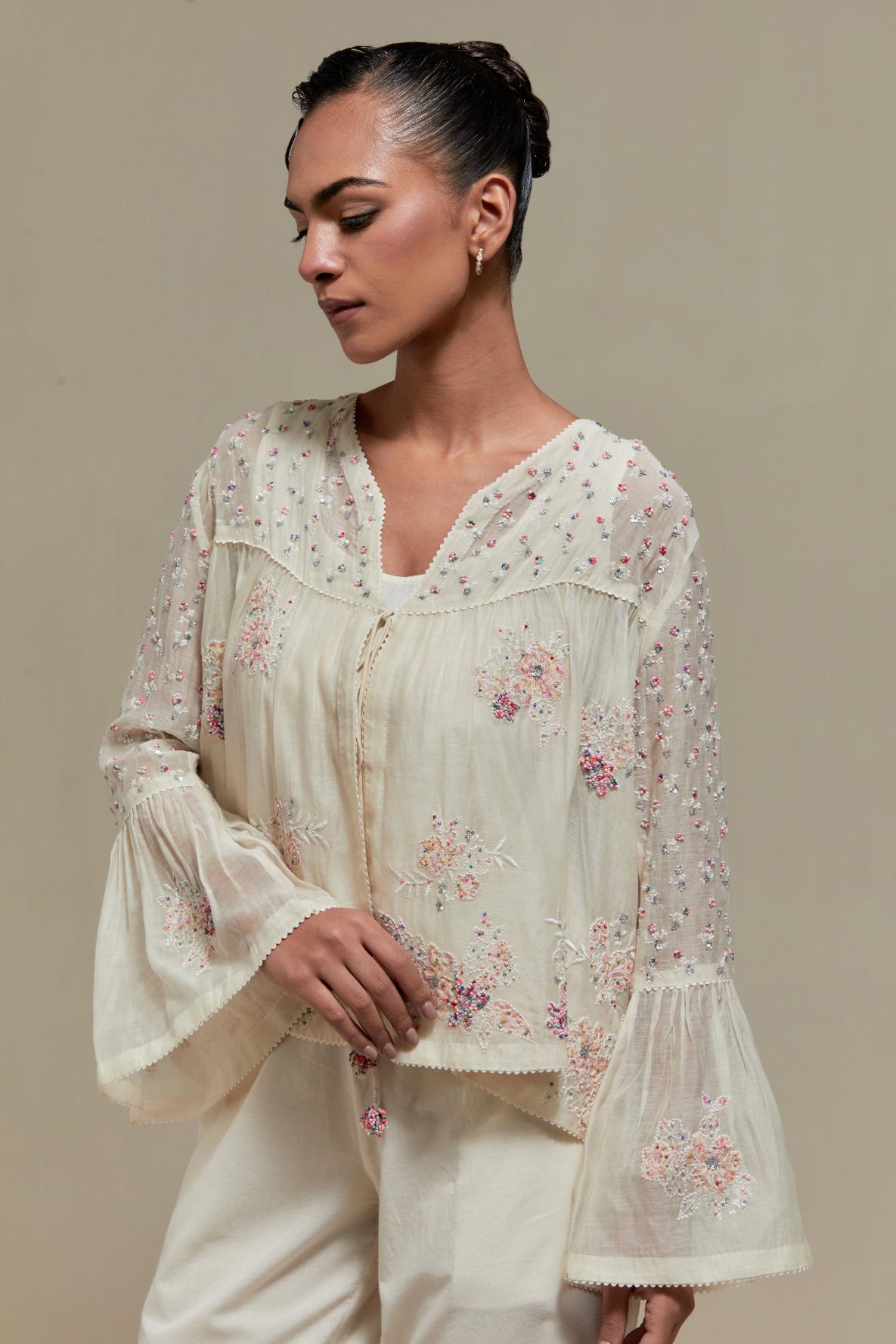 Off-white cotton Chanderi short top featuring pink & beige block print appliqué, floral embroidery, and beadwork. Paired with matching straight pants with side appliqué and sequin highlights. Ideal for elegant, light wear.