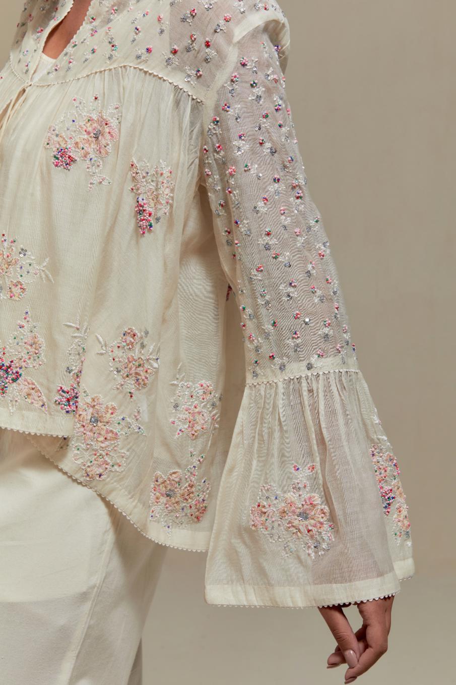 Off-white cotton Chanderi short top featuring pink & beige block print appliqué, floral embroidery, and beadwork. Paired with matching straight pants with side appliqué and sequin highlights. Ideal for elegant, light wear.