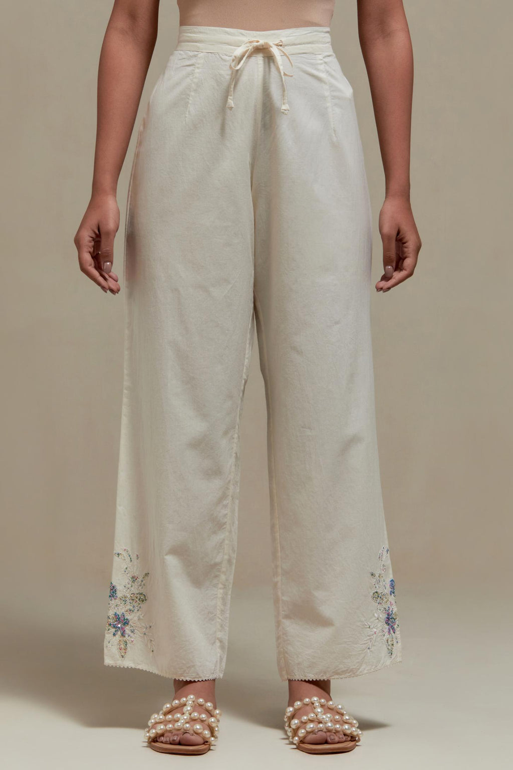 Off white straight pants with blue & beige hand block printed appliqué motifs at the sides, highlighted with sequins and multi coloured beads.