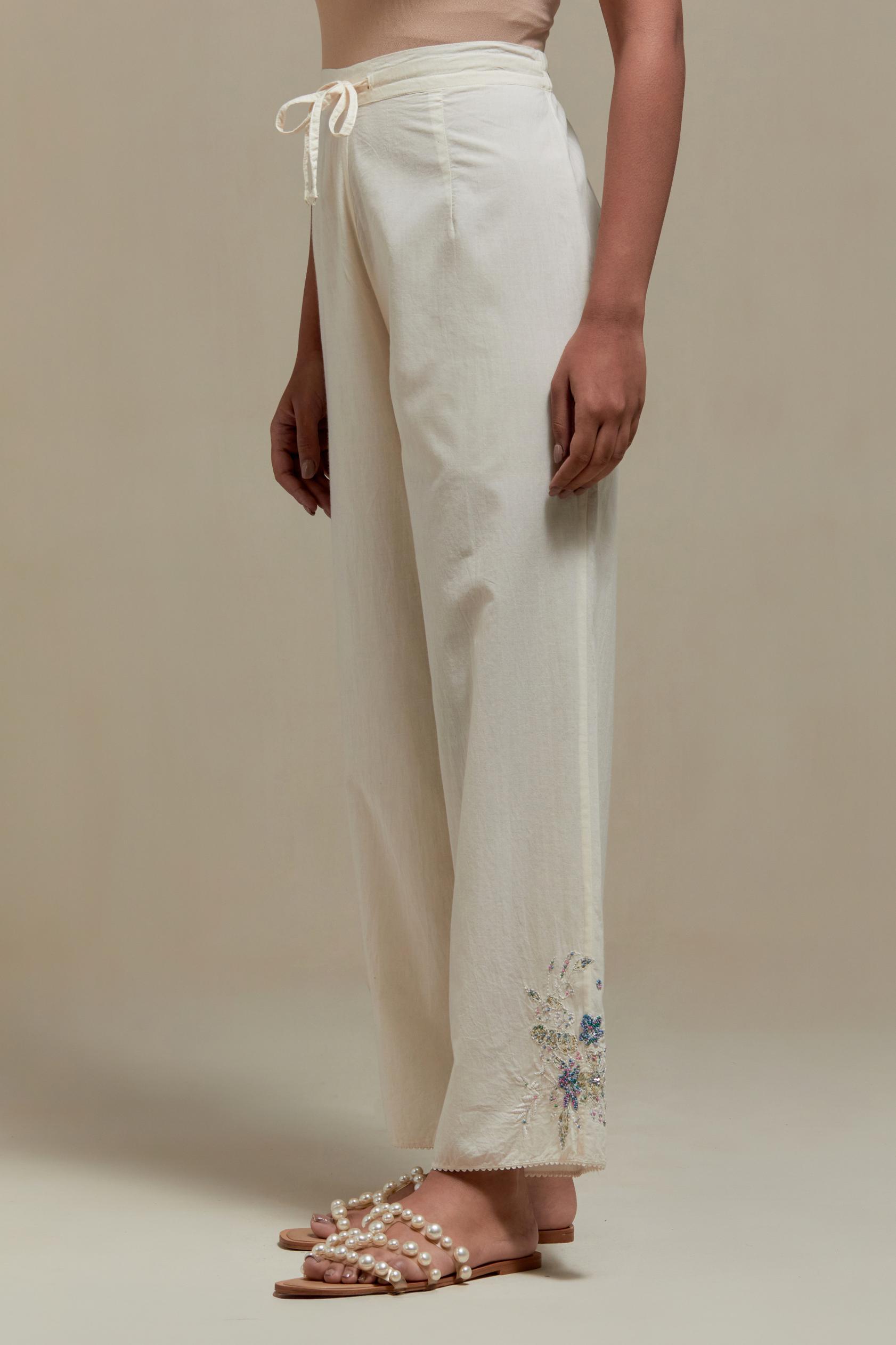 Off white straight pants with blue & beige hand block printed appliqué motifs at the sides, highlighted with sequins and multi coloured beads.