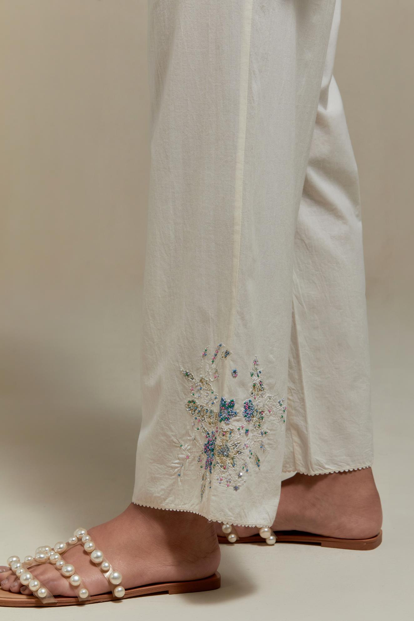Off white straight pants with blue & beige hand block printed appliqué motifs at the sides, highlighted with sequins and multi coloured beads.