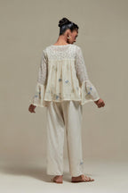 Off-white cotton Chanderi short top with blue & beige block print appliqué, floral embroidery, and beadwork. Paired with straight pants featuring side appliqué and sequin highlights. Elegant, detailed, and handcrafted.