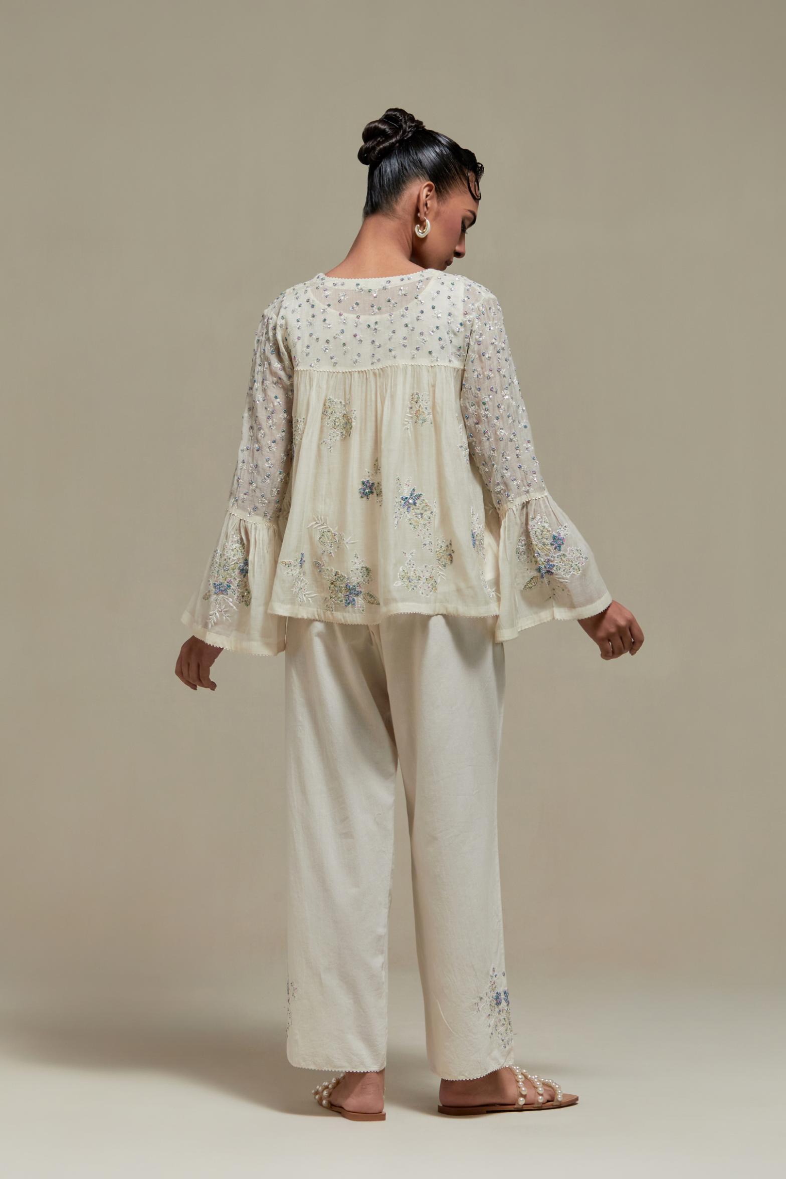 Off-white cotton Chanderi short top with blue & beige block print appliqué, floral embroidery, and beadwork. Paired with straight pants featuring side appliqué and sequin highlights. Elegant, detailed, and handcrafted.