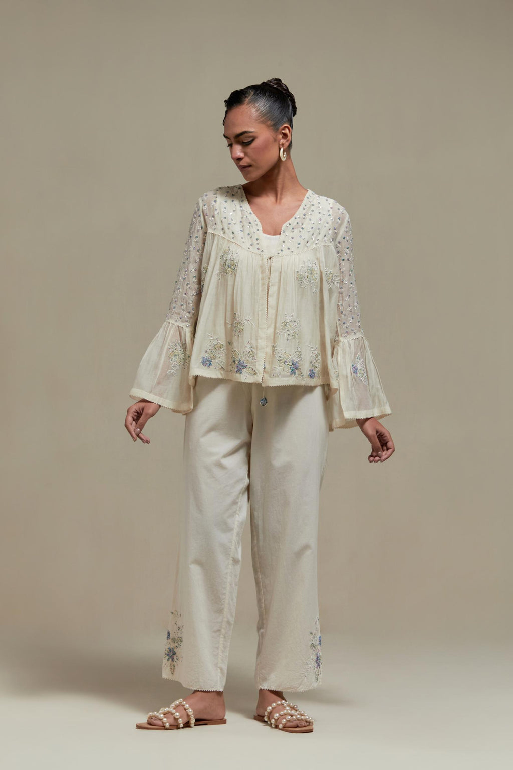 Off-white cotton Chanderi short top with blue & beige block print appliqué, floral embroidery, and beadwork. Paired with straight pants featuring side appliqué and sequin highlights. Elegant, detailed, and handcrafted.