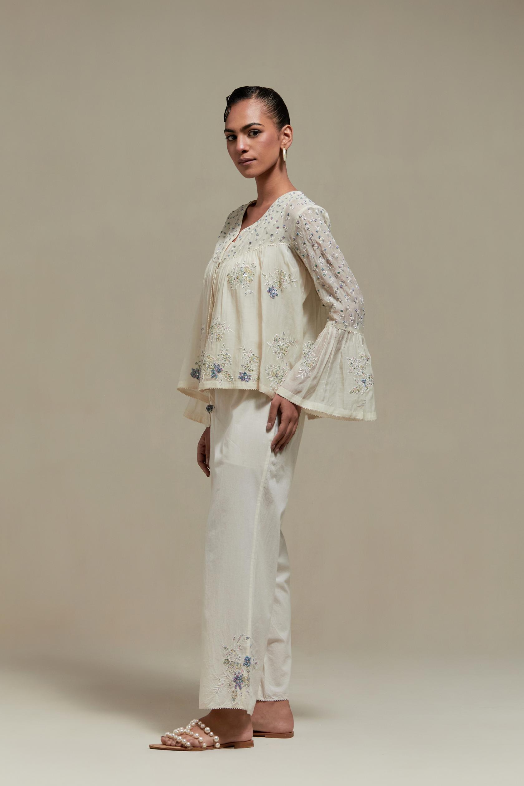 Off-white cotton Chanderi short top with blue & beige block print appliqué, floral embroidery, and beadwork. Paired with straight pants featuring side appliqué and sequin highlights. Elegant, detailed, and handcrafted.