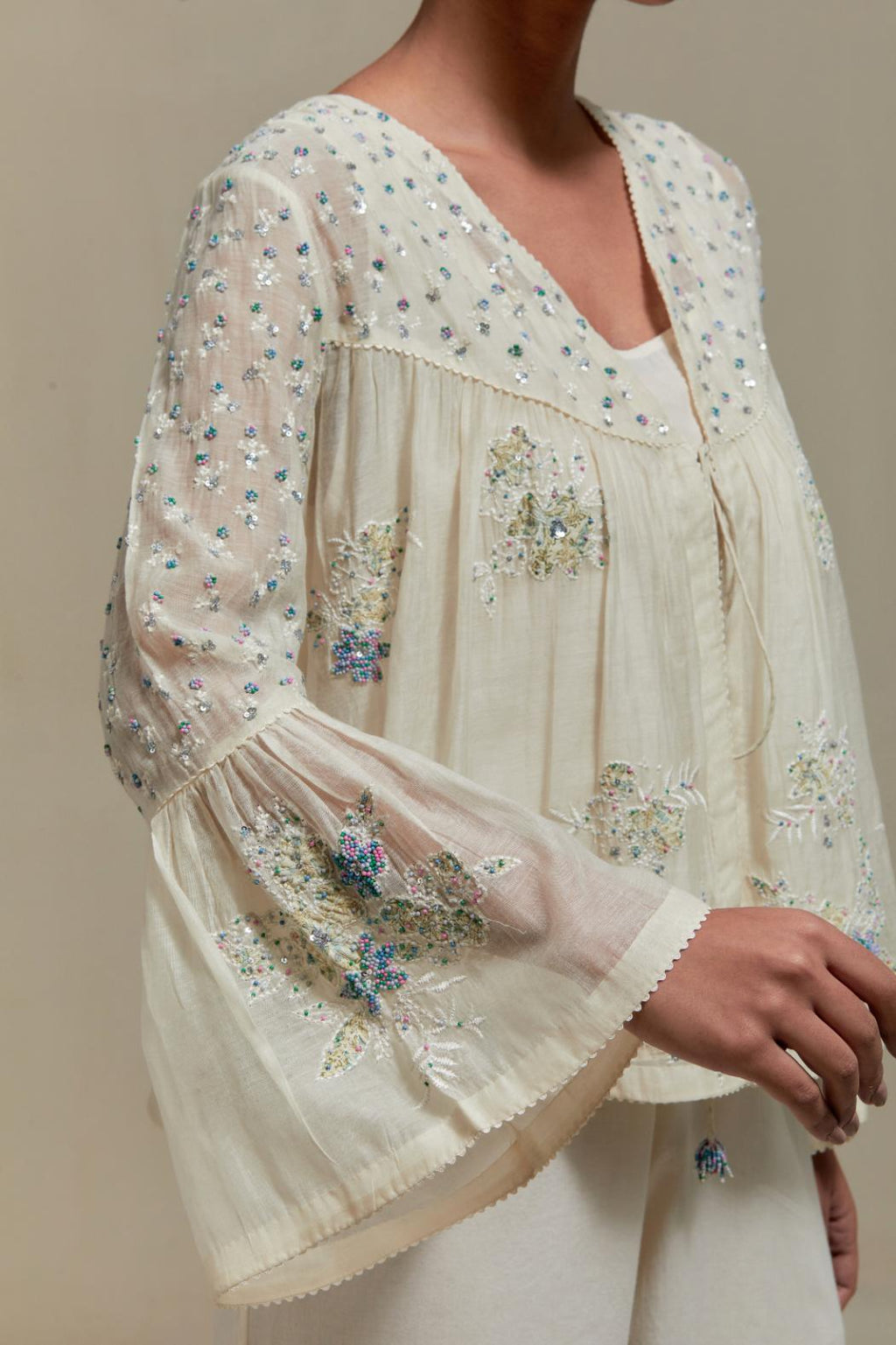 Off-white cotton Chanderi short top with blue & beige block print appliqué, floral embroidery, and beadwork. Paired with straight pants featuring side appliqué and sequin highlights. Elegant, detailed, and handcrafted.