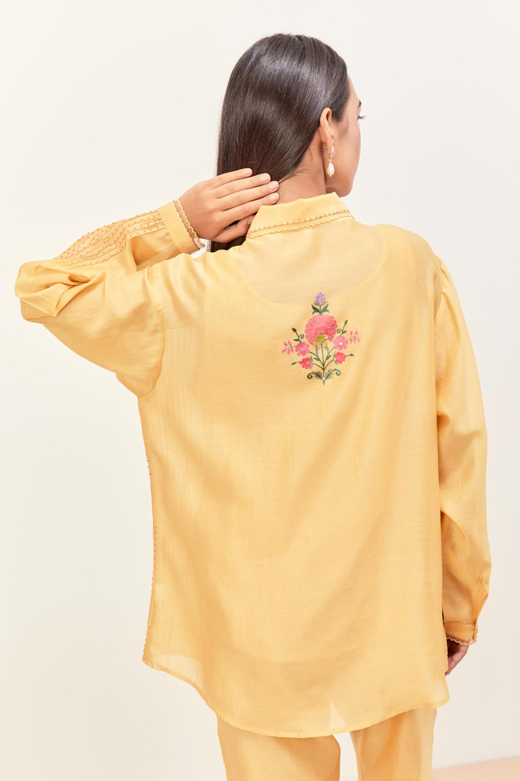 Yellow silk chanderi shirt with all-over pin tucks, highlighted with contrast beads in the front, paired with yellow silk chanderi straight pants detailed with multi colored applique, highlighted with sequins work at bottom hem.