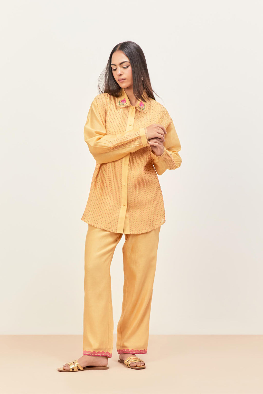Yellow silk chanderi shirt with all-over pin tucks, highlighted with contrast beads in the front, paired with yellow silk chanderi straight pants detailed with multi colored applique, highlighted with sequins work at bottom hem.
