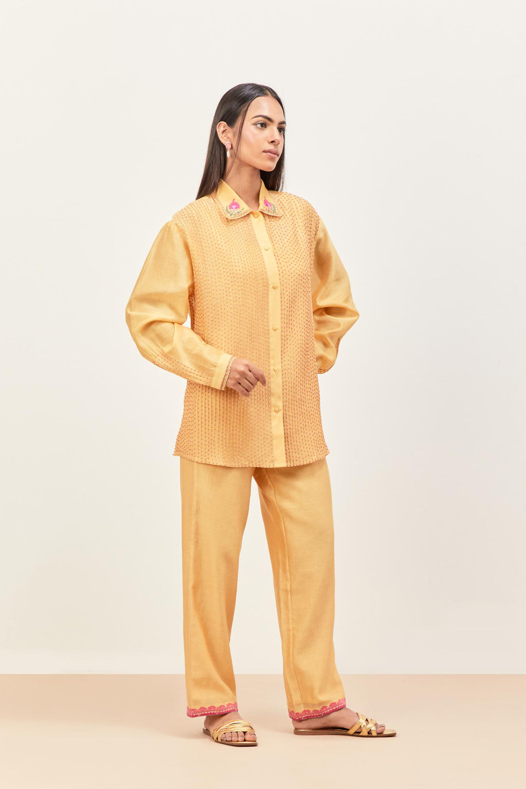 Yellow silk chanderi shirt with all-over pin tucks, highlighted with contrast beads in the front, paired with yellow silk chanderi straight pants detailed with multi colored applique, highlighted with sequins work at bottom hem.