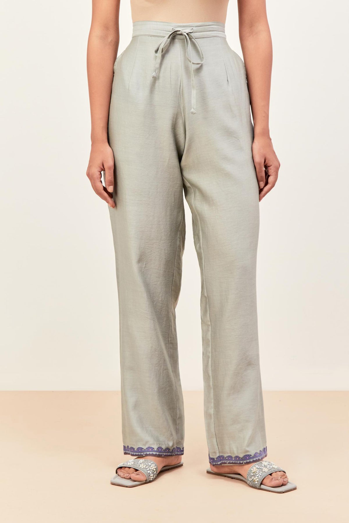 Bluish grey silk chanderi straight pants detailed with multi colored applique, highlighted with sequins work at bottom hem.