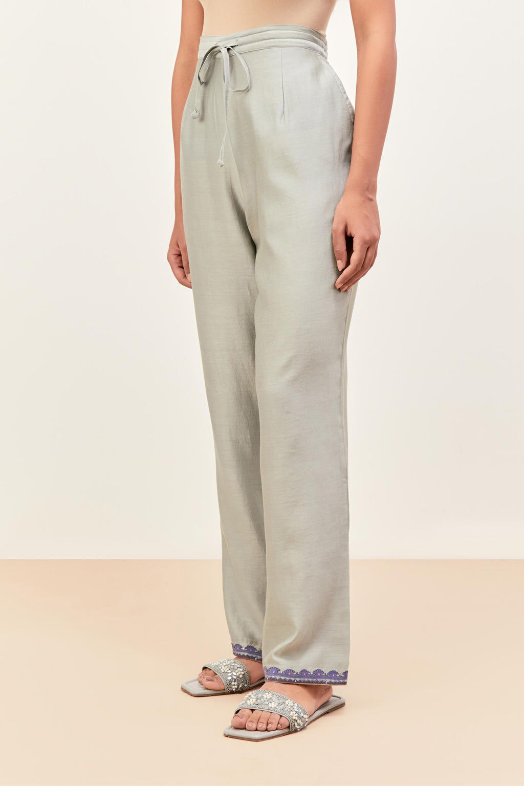 Bluish grey silk chanderi straight pants detailed with multi colored applique, highlighted with sequins work at bottom hem.