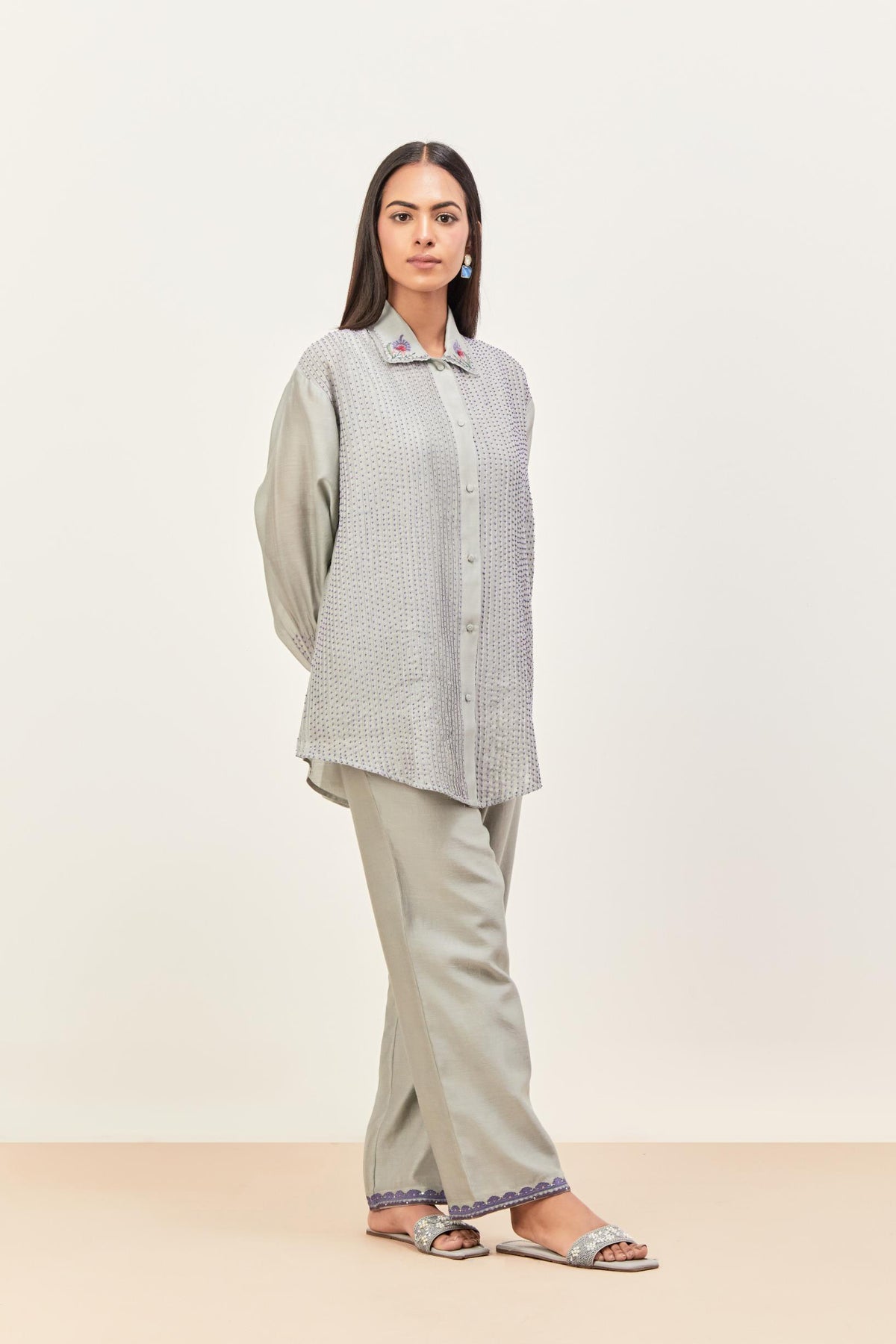 Bluish Grey silk chanderi shirt with all-over pin tucks, highlighted with contrast beads in the front, paired with Bluish Grey silk chanderi straight pants detailed with multi colored applique, highlighted with sequins work at bottom hem.