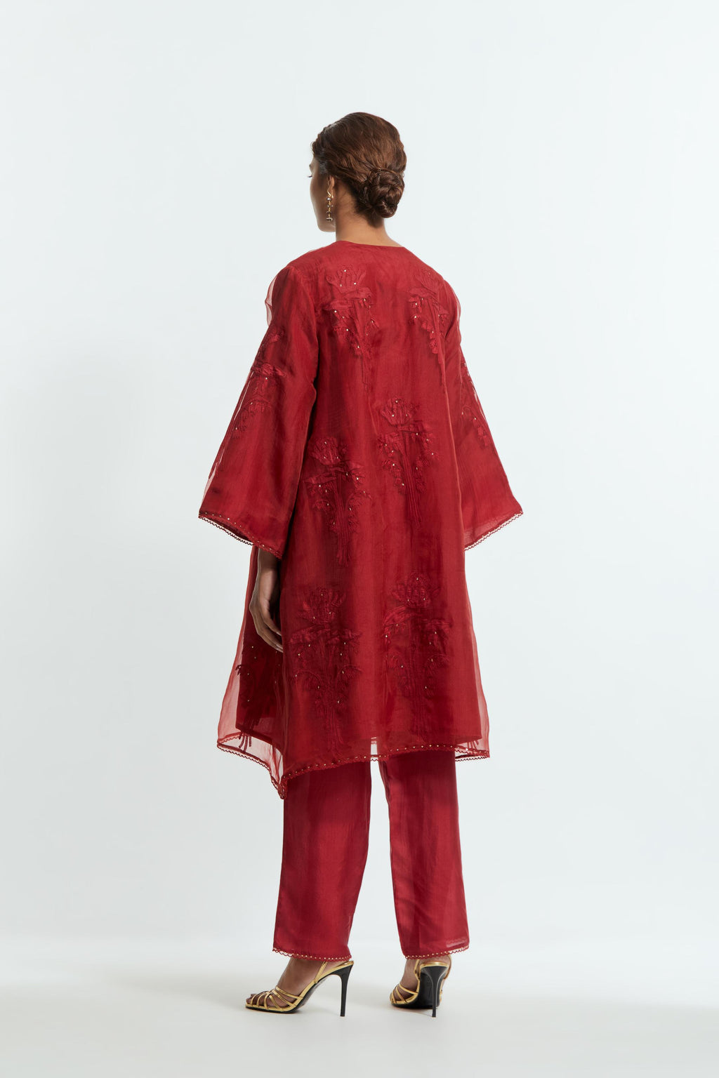 Red silk organza A-line short kurta adorned with delicately placed floral appliqué motifs and subtle sequin embellishments. Paired with red silk straight pants detailed with scalloped organza edging at the hem, highlighted with gold sequins work.
