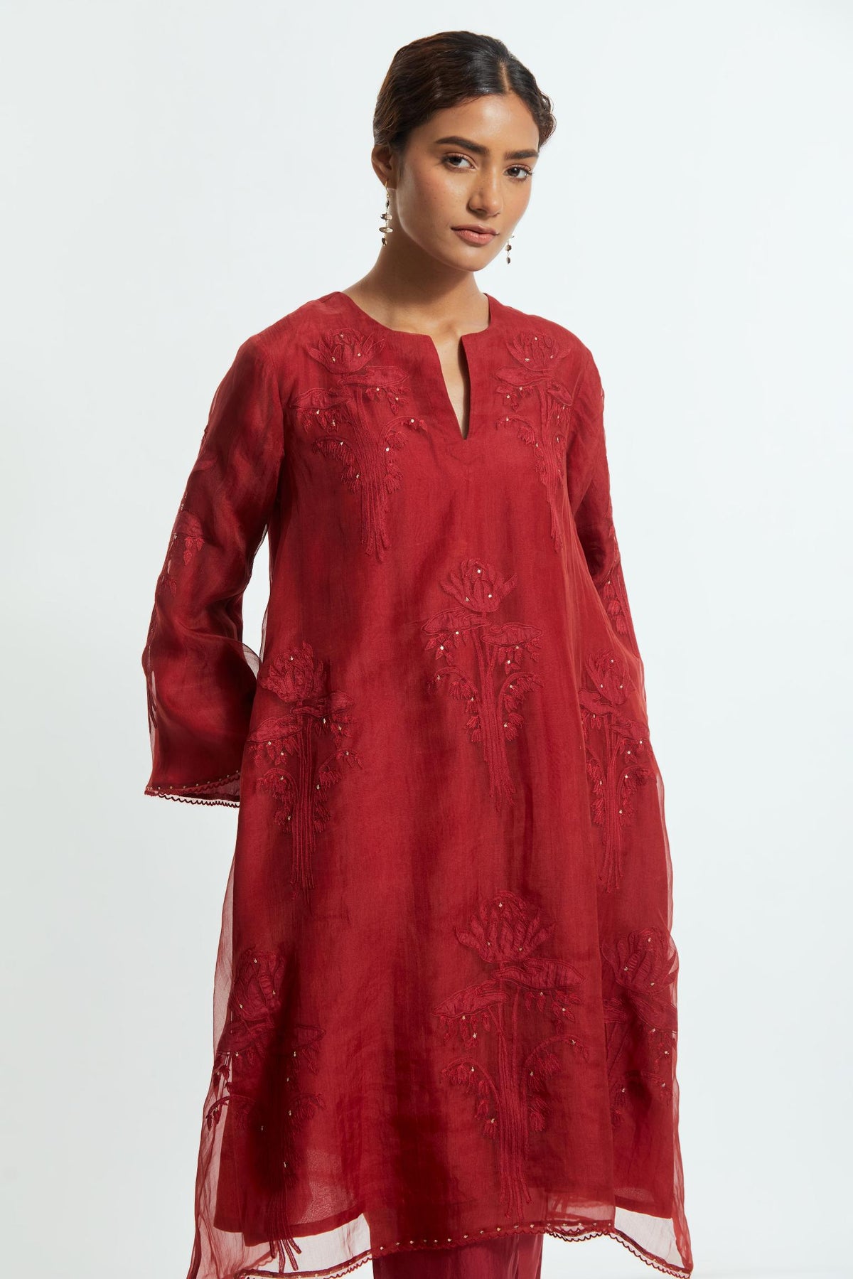 Red silk organza A-line short kurta adorned with delicately placed floral appliqué motifs and subtle sequin embellishments. Paired with red silk straight pants detailed with scalloped organza edging at the hem, highlighted with gold sequins work.