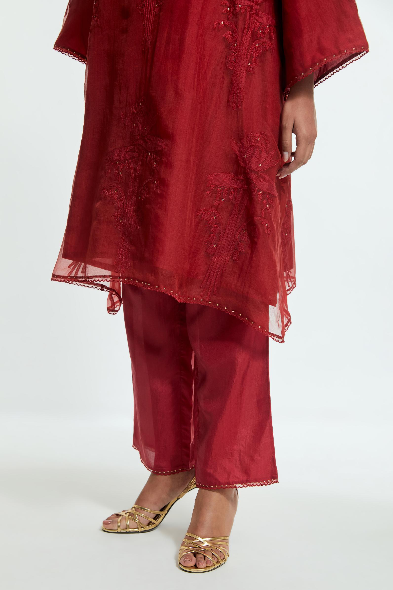 Red silk organza A-line short kurta adorned with delicately placed floral appliqué motifs and subtle sequin embellishments. Paired with red silk straight pants detailed with scalloped organza edging at the hem, highlighted with gold sequins work.