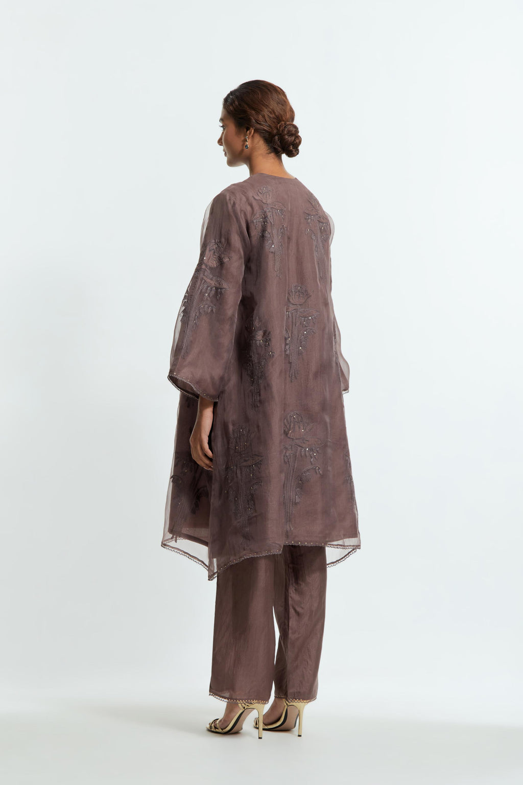 Grey silk organza A-line short kurta adorned with delicately placed floral appliqué motifs and subtle sequin embellishments. Paired with grey silk straight pants detailed with scalloped organza edging at hem, delicately highlighted with gold sequins work.