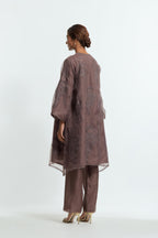 Grey silk organza A-line short kurta adorned with delicately placed floral appliqué motifs and subtle sequin embellishments. Paired with grey silk straight pants detailed with scalloped organza edging at hem, delicately highlighted with gold sequins work.