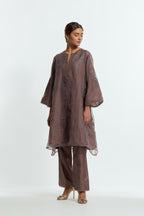 Grey silk organza A-line short kurta adorned with delicately placed floral appliqué motifs and subtle sequin embellishments. Paired with grey silk straight pants detailed with scalloped organza edging at hem, delicately highlighted with gold sequins work.