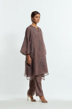 Grey silk organza A-line short kurta adorned with delicately placed floral appliqué motifs and subtle sequin embellishments. Paired with grey silk straight pants detailed with scalloped organza edging at hem, delicately highlighted with gold sequins work.