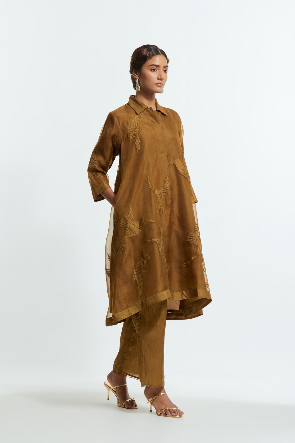 Olive silk organza A-line short kurta featuring appliqué bird motifs gracefully placed across the front, back and sleeves. Paired with Olive silk straight pants detailed with scalloped organza edging at the hem, delicately highlighted with tonal beadwork.