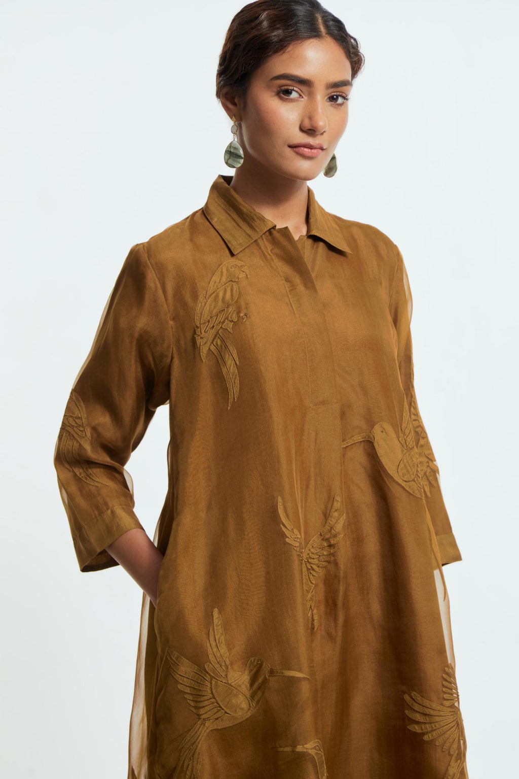 Olive silk organza A-line short kurta featuring appliqué bird motifs gracefully placed across the front, back and sleeves. Paired with Olive silk straight pants detailed with scalloped organza edging at the hem, delicately highlighted with tonal beadwork.