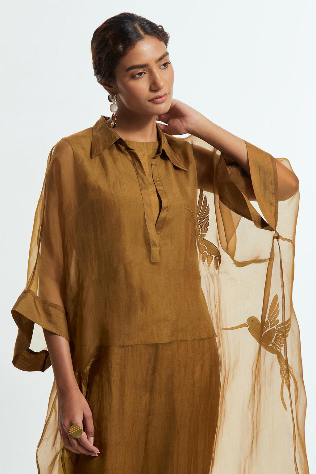 Olive silk organza kaftan with a sheer finish, delicately adorned with appliqué bird motifs along the hem and sides. Paired with Olive silk straight pants detailed with scalloped organza edging at the hem, delicately highlighted with tonal beadwork.