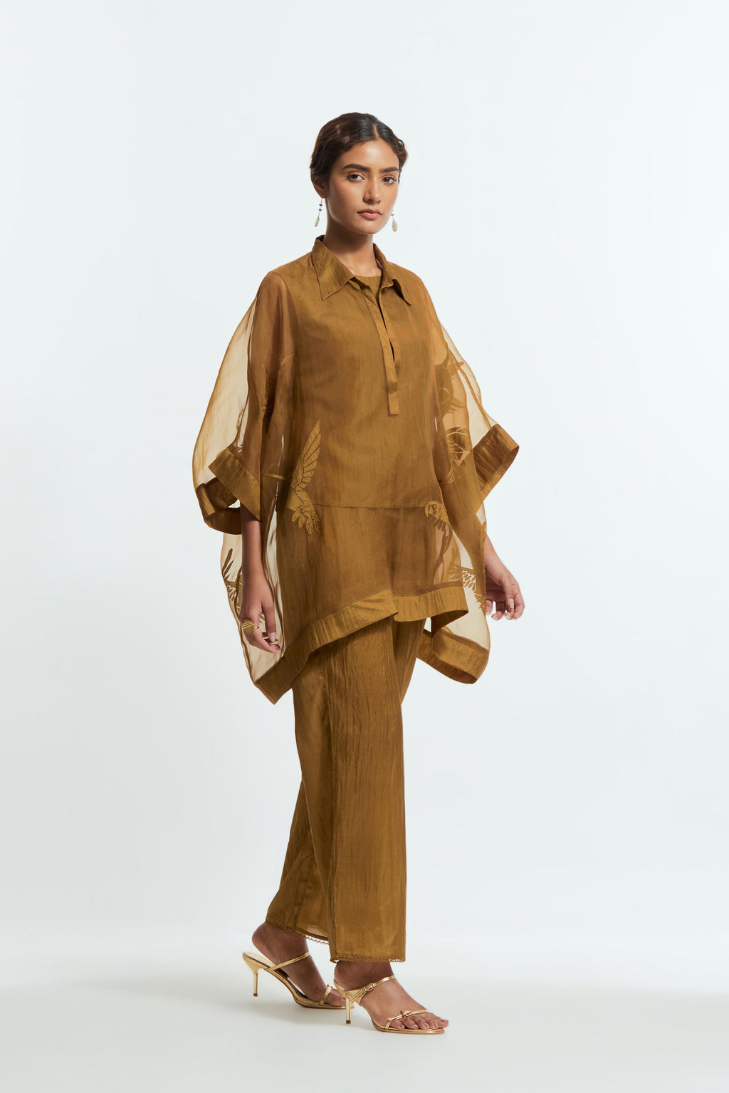 Olive silk organza short kaftan top with a sheer finish, delicately adorned with appliqué bird motifs along the hem and sides. Paired with olive silk straight pants detailed with scalloped organza edging at hem, delicately highlighted with tonal beadwork.