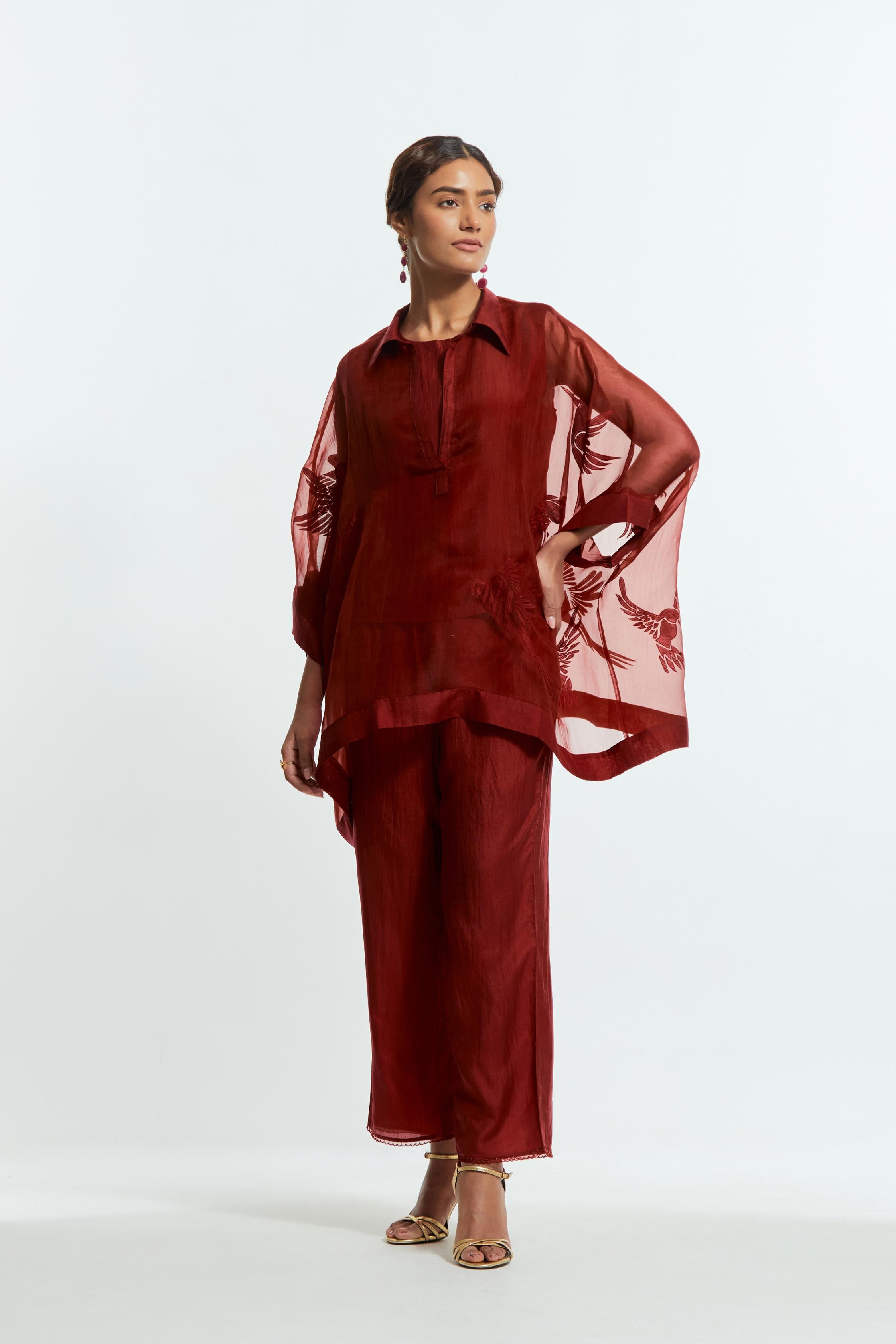 Red silk organza short kaftan top with a sheer finish, delicately adorned with appliqué bird motifs along the hem and sides. Paired with Red silk straight pants detailed with scalloped organza edging at the hem, delicately highlighted with tonal beadwork.