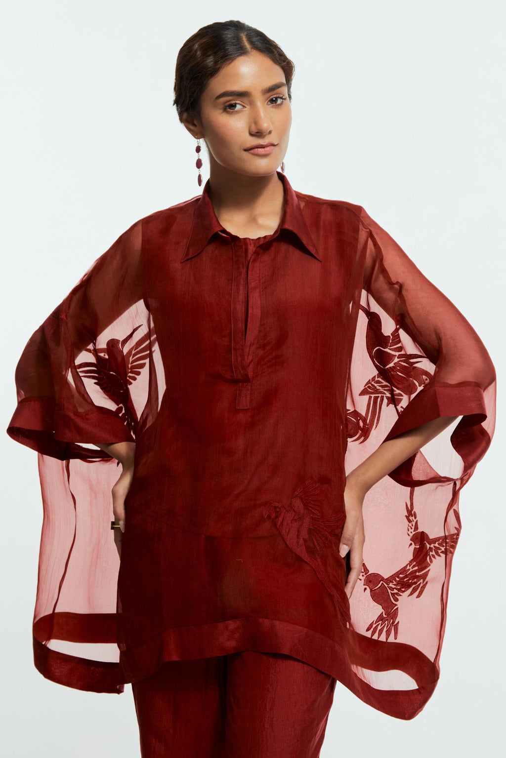 Red silk organza short kaftan top with a sheer finish, delicately adorned with appliqué bird motifs along the hem and sides. Paired with Red silk straight pants detailed with scalloped organza edging at the hem, delicately highlighted with tonal beadwork.